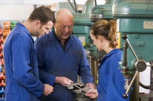 Three machinists in workspace by machine talking